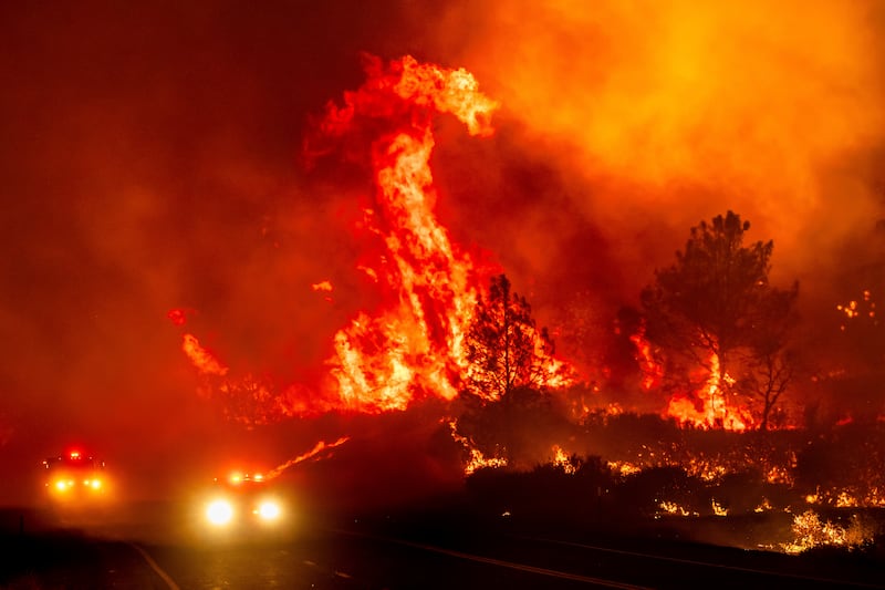 Flames leap above fire vehicles driving along a road in Tehama County, California (Noah Berger/AP)