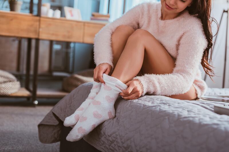 Young woman sitting on a bed putting on fluffy socks