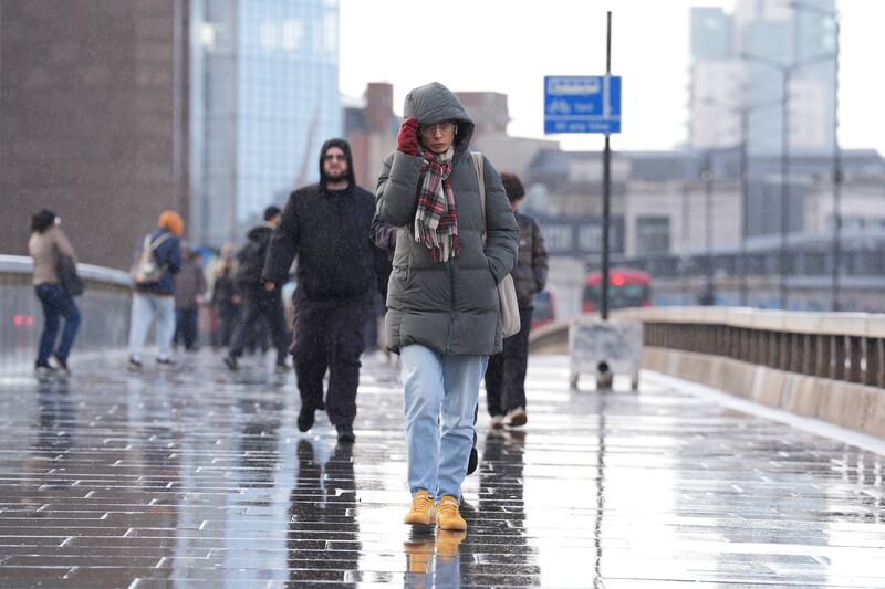 People shelter from the rain as they walk across London Bridge in central London