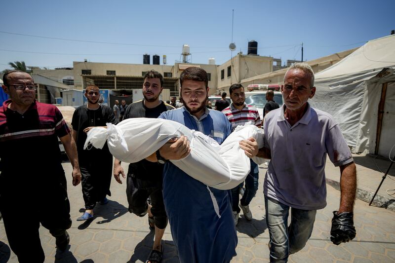 A Palestinian man holds the body of a child killed in the Israeli bombardment of the Gaza Strip (Abdel Kareem Hana/AP)