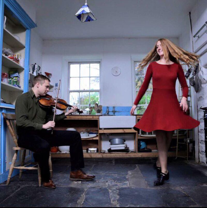 A photpgraph of Ciarán Ó Maonaigh playing the fiddle while Caitlín Nic Gabhann dances in a red dress