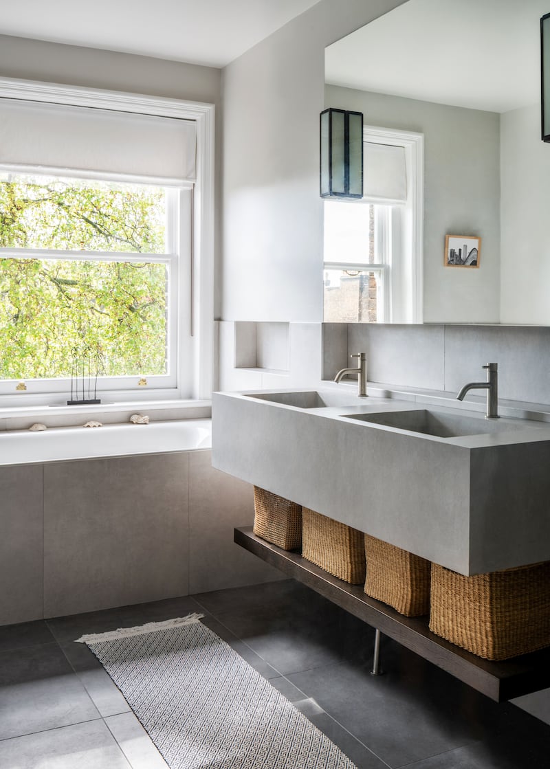 A bespoke vanity unit with spacious double sinks adds style and ample storage space with shelving for wicker baskets in this bathroom by Aflux Designs