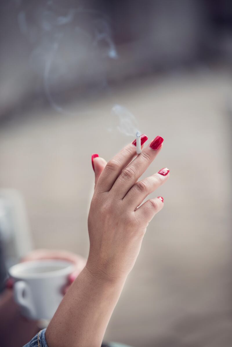 Woman drinking cup of coffee and smoking a cigarette