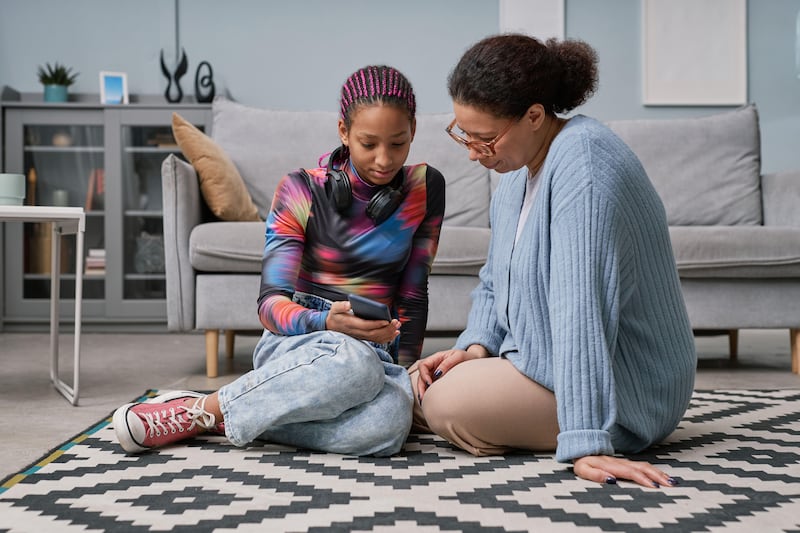 Teenage girl sat on the floor with her mum looking through her phone