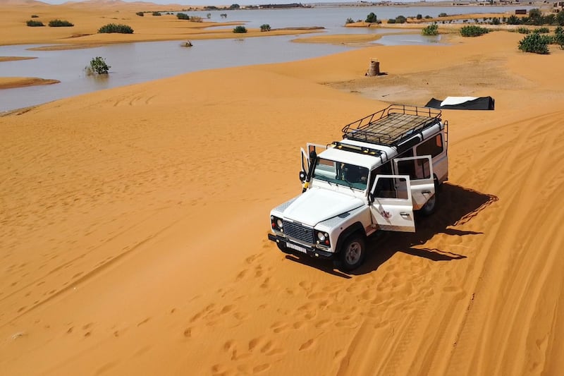 A 4×4 vehicle transports tourists on sand dunes next to a lake caused by heavy rain in the desert in south-eastern Morocco (AP)