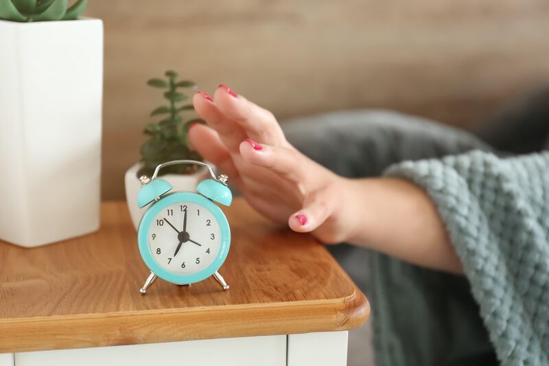 A woman’s hand emerging from under a duvet to turn off an alarm clock