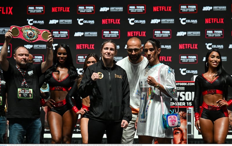 Katie Taylor and Amanda Serrano starring into the crowd with people standing behind them at a press conference