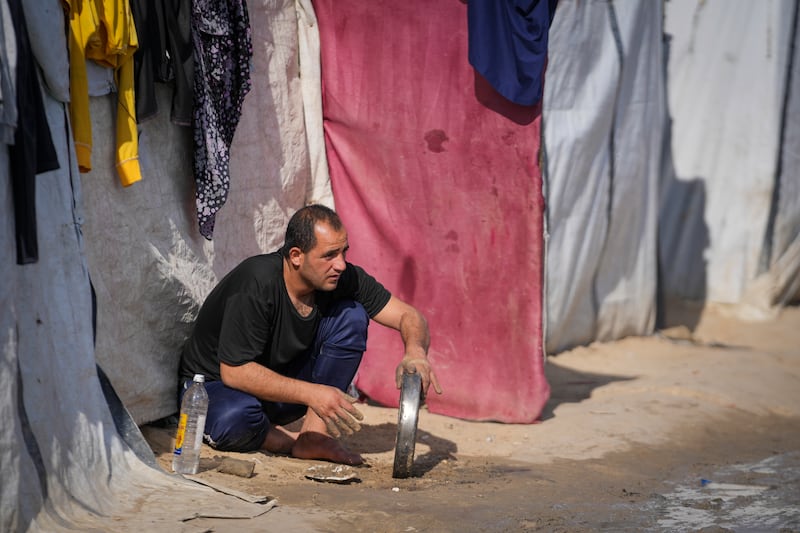 A man washes a tray outside a tent at a camp for displaced Palestinians in Deir al-Balah, central Gaza Strip (Abdel Kareem Hana/AP)