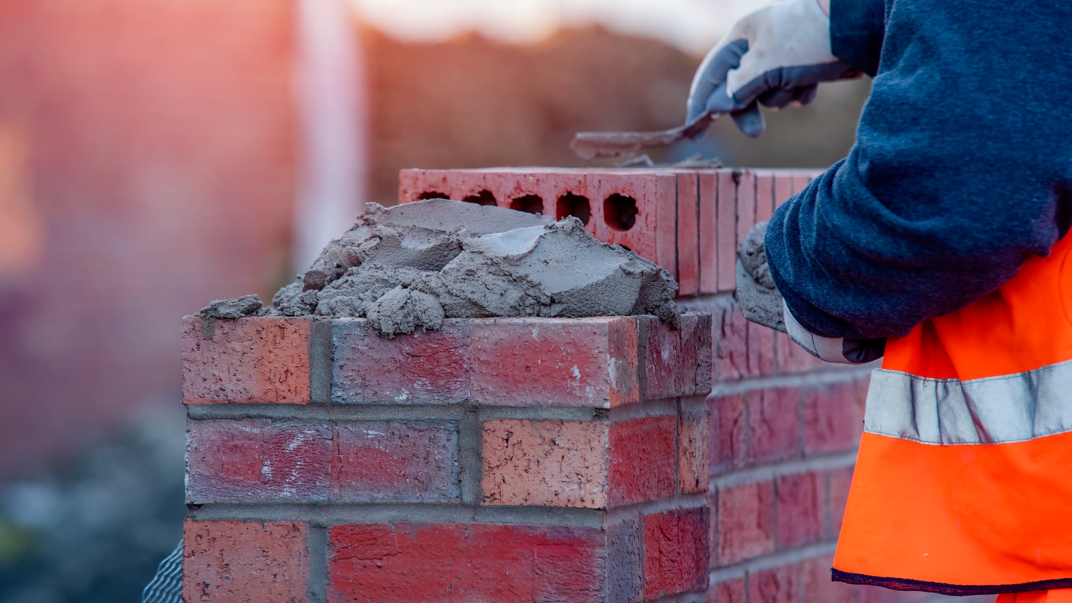 Close up of industrial bricklayer laying bricks on cement mix on construction site