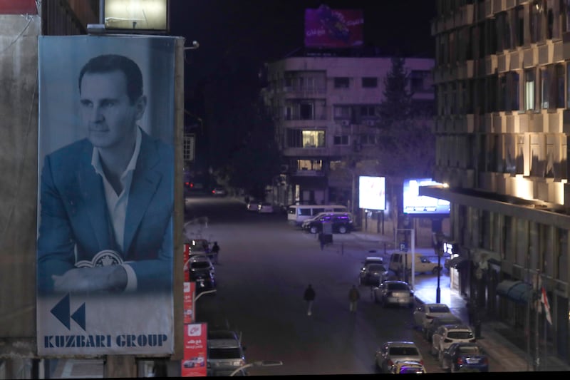 A giant banner of Syrian President Bashar Assad hangs on the facade of a building, as pedestrian walk through an the empty streets of Damascus (Omar Sanadiki/AP)