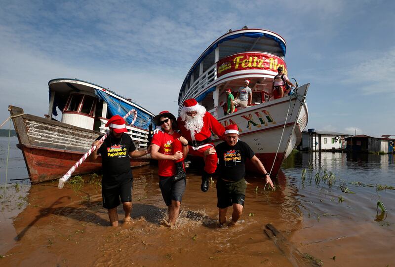 Jorge Barroso, dressed as Santa Claus, is carried by his helpers after arriving on a boat to distribute Christmas gifts to children who live in the riverside communities of the Amazon (Edmar Barros/AP)