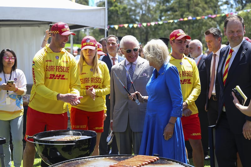 Charles and Camilla laugh as they turn some sausages during the community barbecue