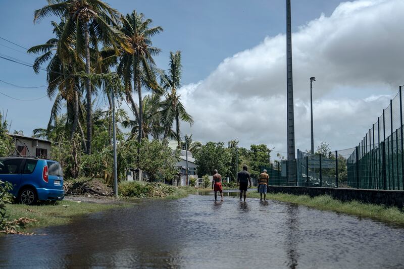 Men walk on a submerged street in the town of Saint-Paul, on the French Indian Ocean island of Reunion (Lewis Joly/AP)