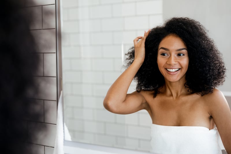 Young woman with curly dark hair looking in the mirror smiling