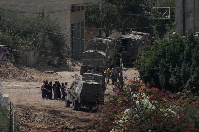 Palestinians next to Israeli armoured vehicles during a military operation in the West Bank Jenin refugee camp on Saturday (Majdi Mohammed/AP)