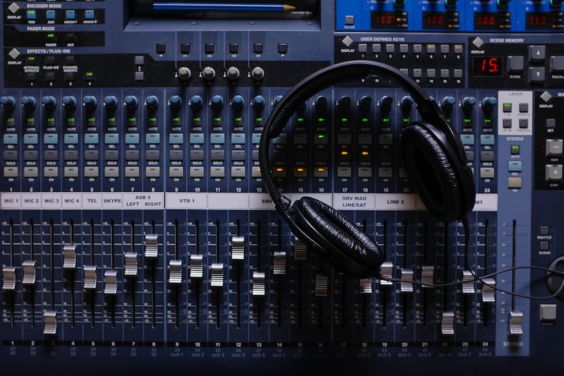 Headphones, Amplifying Equipment, Studio Audio Mixer Knobs, And Faders. Sound Engineering Equipment. Selective Focus. The photo is covered in sand and noise.