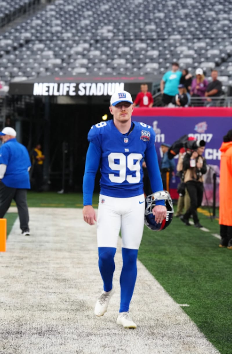 Jude McAtamney walking onto the sideline at MetLife Stadium before the New York Giants took on the Detroit Lions with his helmet in his hand and a cap on his head wearing number 99