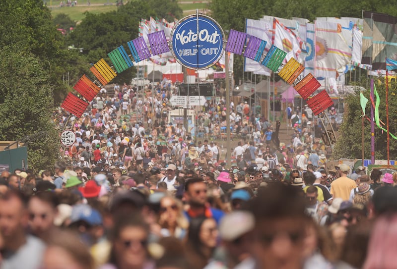 Festival-goers walking under a sign saying ‘Vote Out to Help Out’ at Glastonbury