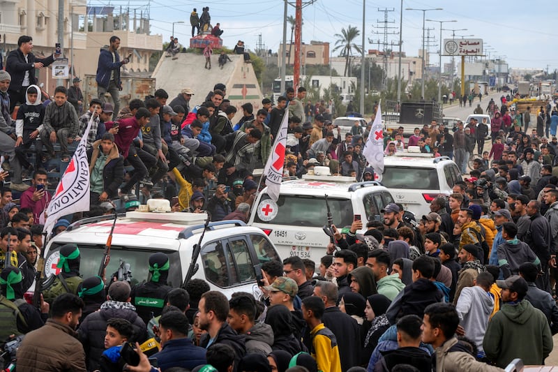 Palestinians gather as Hamas fighters escort Red Cross vehicles (Abdel Kareem Hana/AP)