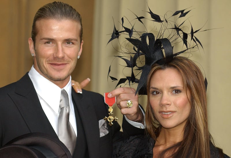 Then-England football captain David Beckham stands with his wife, Victoria, as he shows off the OBE