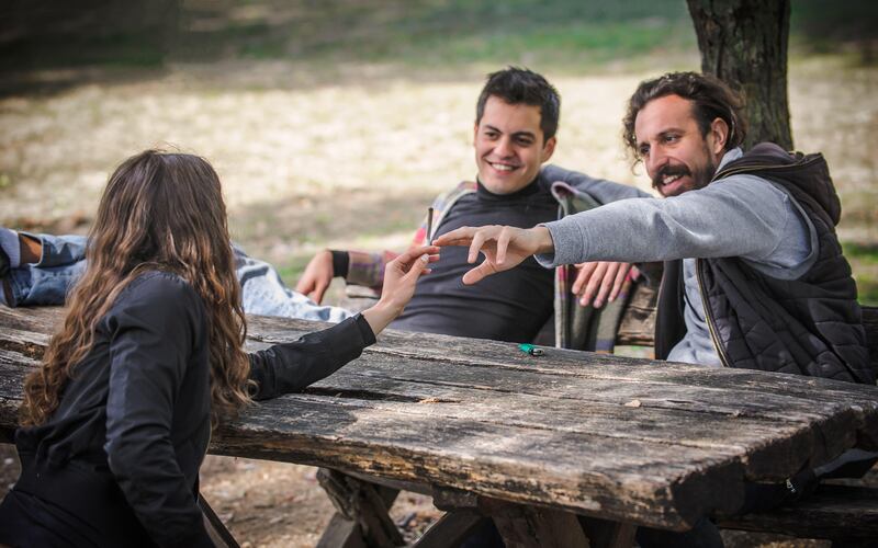 Friends sat around a bench in a park handing each other a cigarette