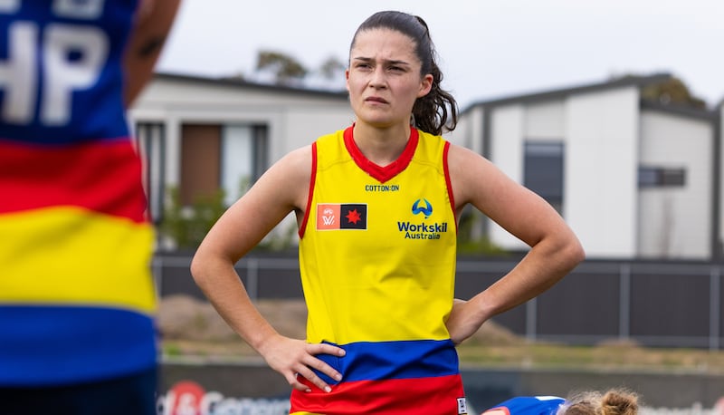 A woman standing with her hands on her hips listening to a coach in a yellow jersey with red and blue stripes