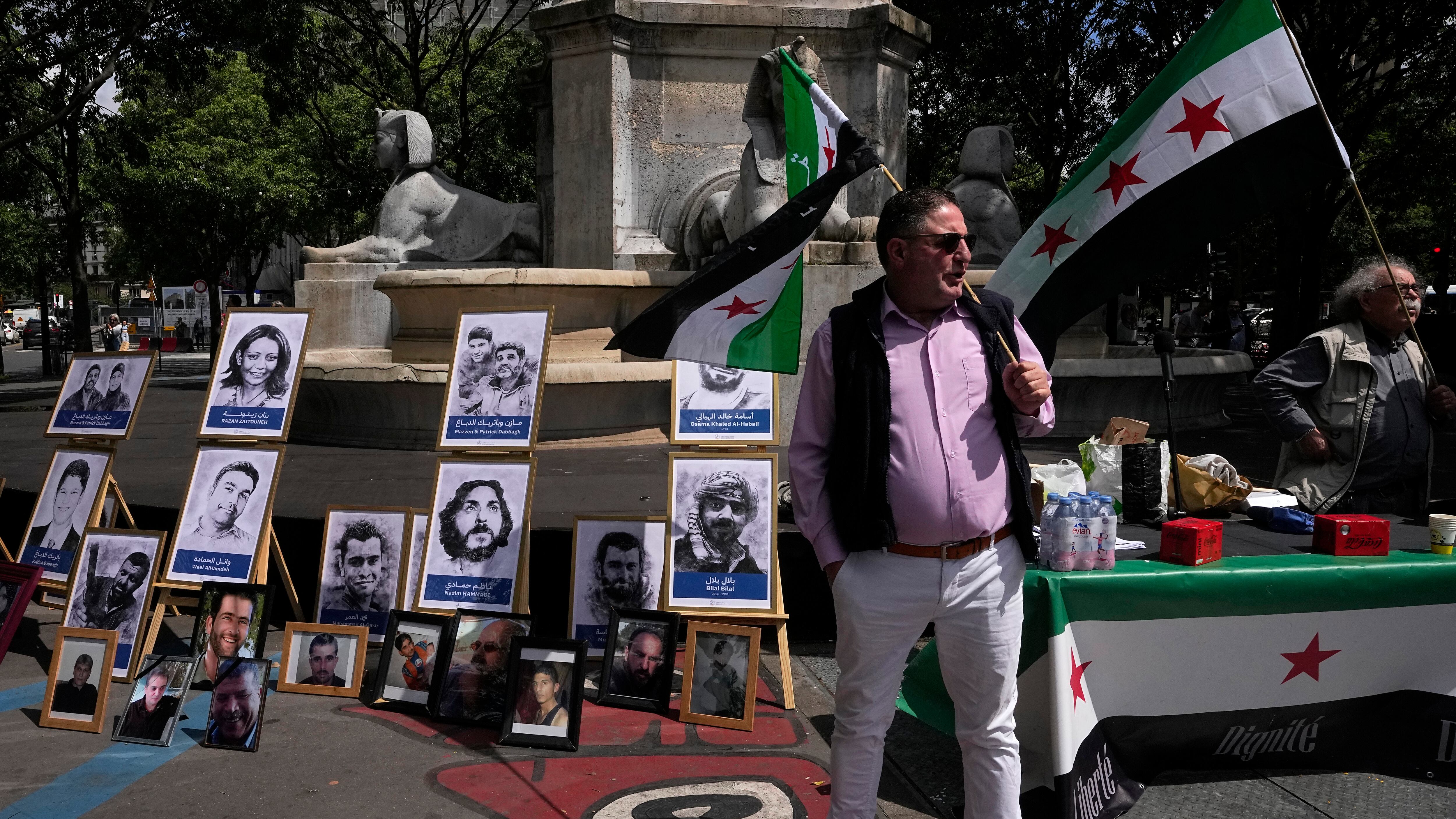 Activists hold Syrian flags next to portraits of alleged victims of the Syrian regime, during a demonstration at a court in Paris (Michel Euler/AP)