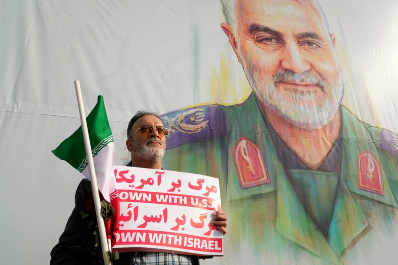 A man holds an anti-US and anti-Israeli placard and an Iranian flag in front of a portrait of the late Iranian Revolutionary Guard general Qassem Soleimani (Vahid Salemi/AP)