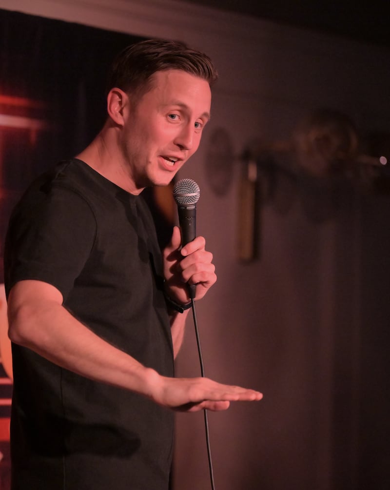 Male stand-up comedian gestures on stage while holding microphone