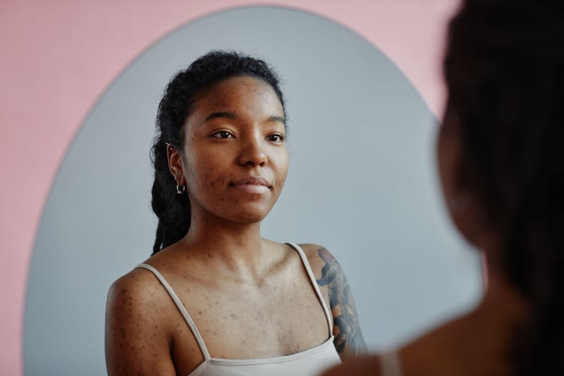 2MNG49A Young black woman with tattoos and acne scars looking in mirror smiling