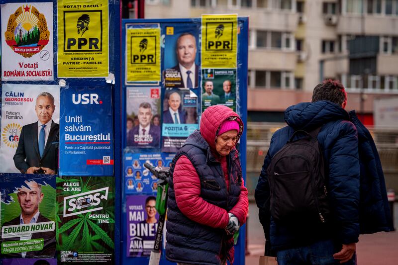 People walk past panels displaying electoral posters ahead of the presidential elections in Bucharest, Romania (Andreea Alexandru/AP)