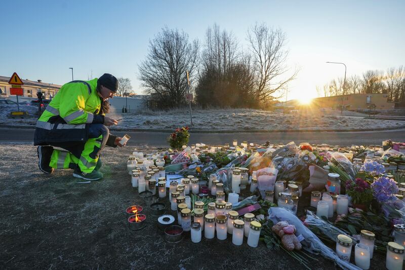 A man lights a candle at a makeshift memorial near the scene of a shooting at an adult education centre (Sergei Grits/AP)