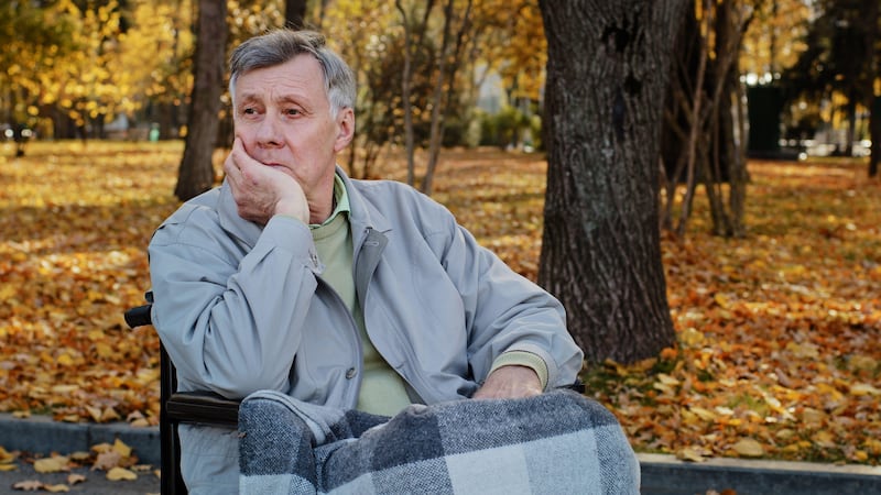 Senior man sitting alone in a wheelchair in a park during autumn looking depressed