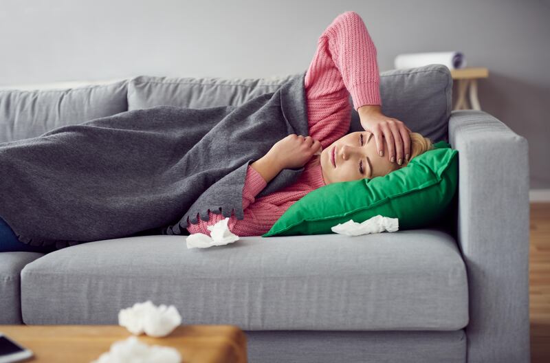 Sick woman lying on the sofa in living room surrounded by snotty tissues