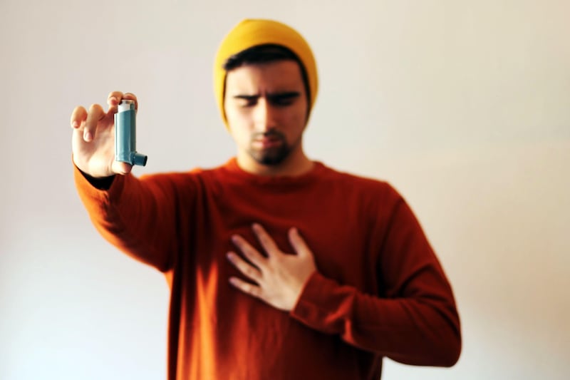 A male feeling wheezy holding a blue inhaler