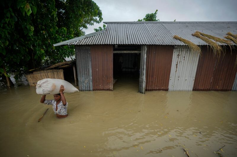 A flood victim carries a sack of rice from his submerged house in Sildubi village in Morigaon district in the northeastern state of Assam, India (Anupam Nath/AP)