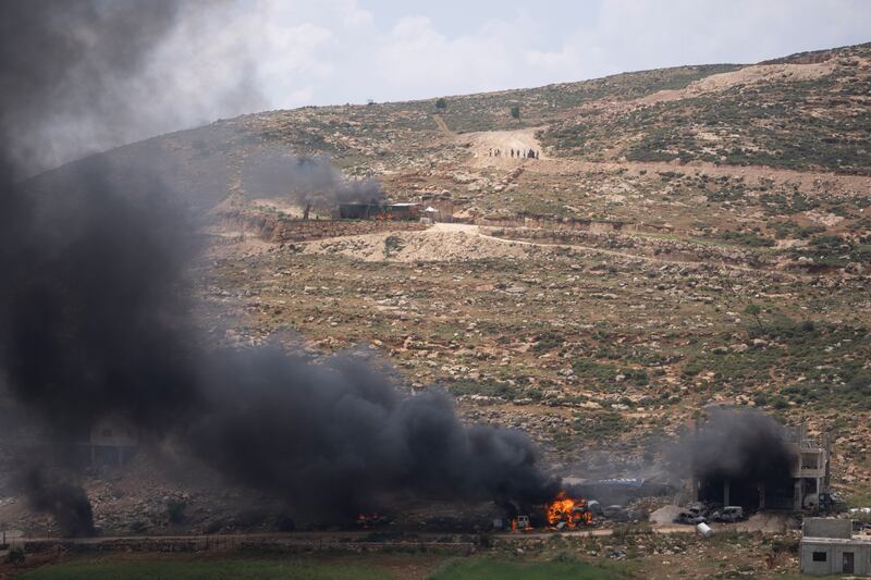 Israeli settlers gather near burning properties of Palestinian villagers (Nasser Nasser/AP)