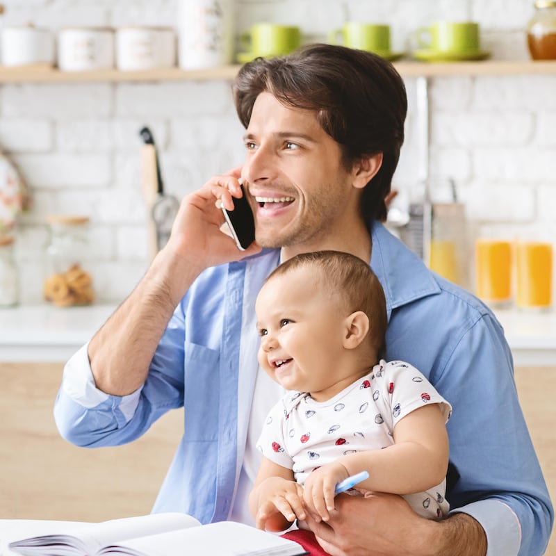 Young man talking on a phone while looking after a baby