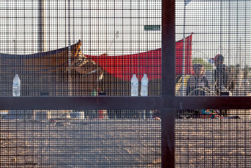 Two migrants, part of a small group, are seen through the mesh of the border fence (Andres Leighton/AP)