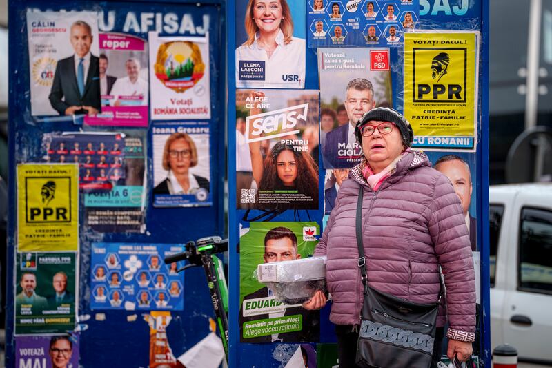 A woman stands by panels displaying electoral posters ahead of the November 24 presidential elections (Andreea Alexandru/AP)