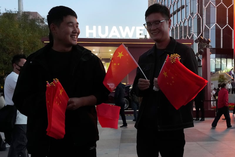 Chinese men hand out national flags during national day holidays near a Huawei pop up store in Beijing (Ng Han Guan/AP)