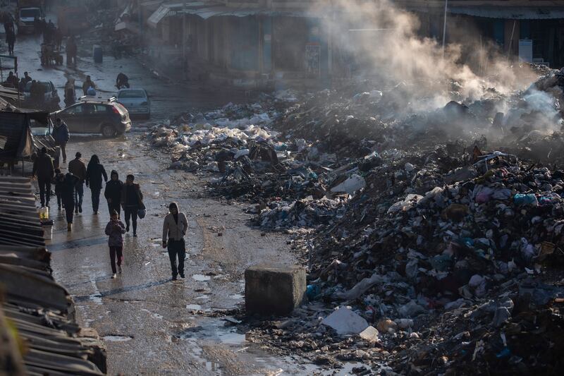 Palestinians walk past a pile of burning rubbish in Gaza City (Jehad Alshrafi/AP)