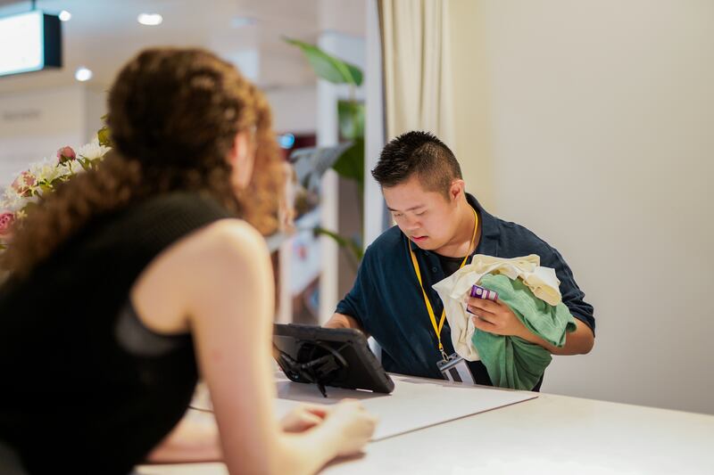 A Sales Assistant with Down’s Sydnrome processes a purchase for a customer in a shop. (Business Disability Forum)