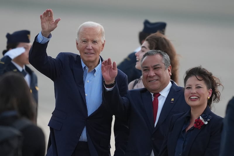 US president Joe Biden, left, Peru’s prime minister Gustavo Adrianzen, centre, and US ambassador to Peru Stephanie Syptak-Ramnath wave on the airport tarmac ahead of the Apec summit (AP/Guadalupe Pardo)