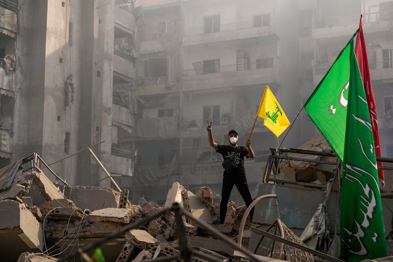 A man flashes the victory sign as holds up a Hezbollah flag on the ruins of a destroyed apartment at the site of an Israeli airstrike in Dahiyeh, Beirut (Hassan Ammar/AP)