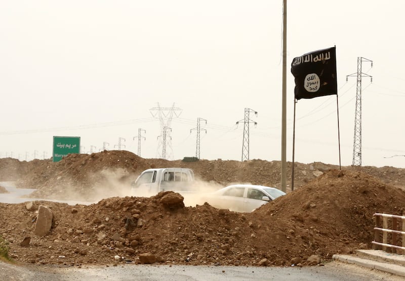 Islamic State militants pass a checkpoint bearing the group’s trademark black flag in 2014 (Hadi Mizban/AP)